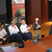 Four panelists and a moderator engaged in a discussion in front of the AVANT Project roll-up